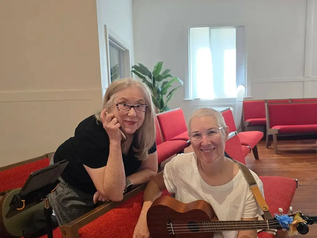 Two players leaning on the back of a pew with a ukulele