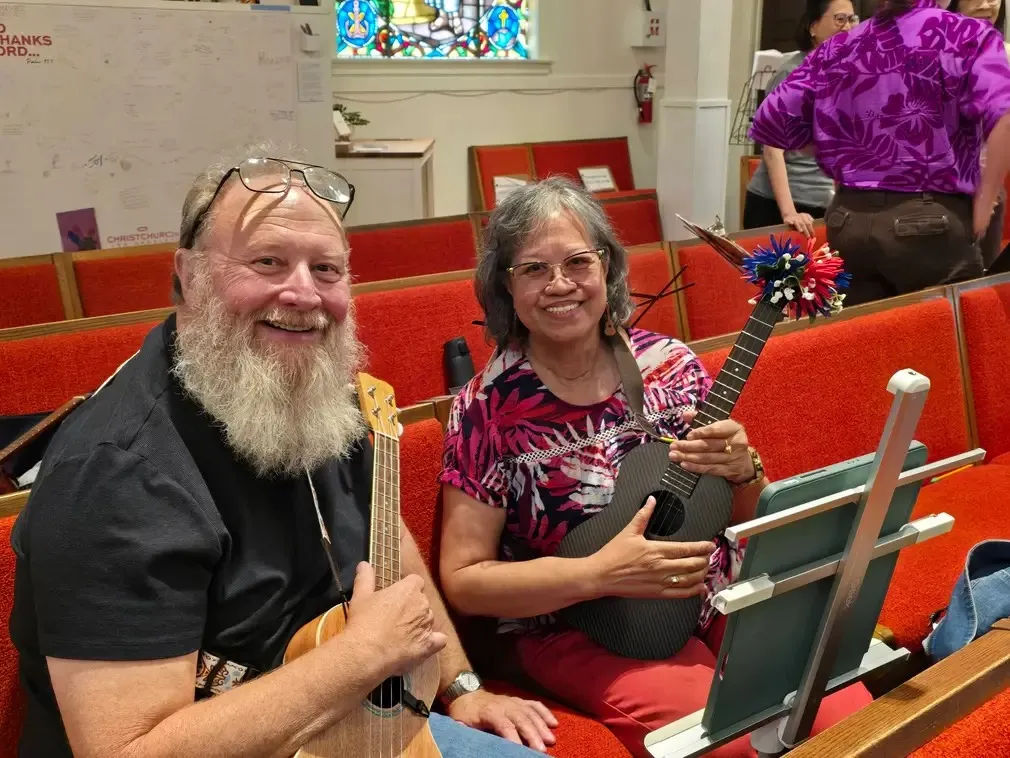Two players side by side in the red pews with ukuleles